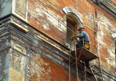 Builders refurbishing the exterior of a heritage-style building.